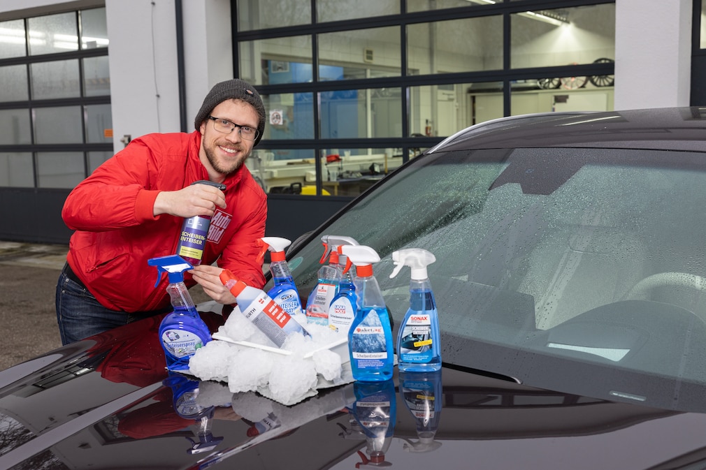 Redakteur sprüht Scheiben-Enteiser, auf der Motorhaube platziert alle getesteten Produkte.