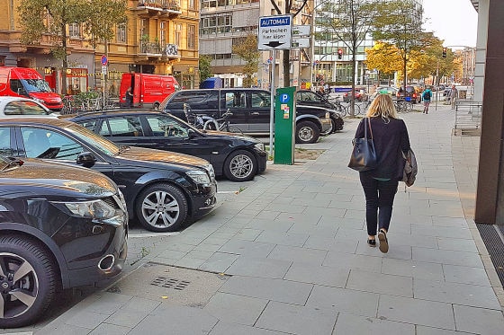 Fußgängerin geht neben parkenden Autos