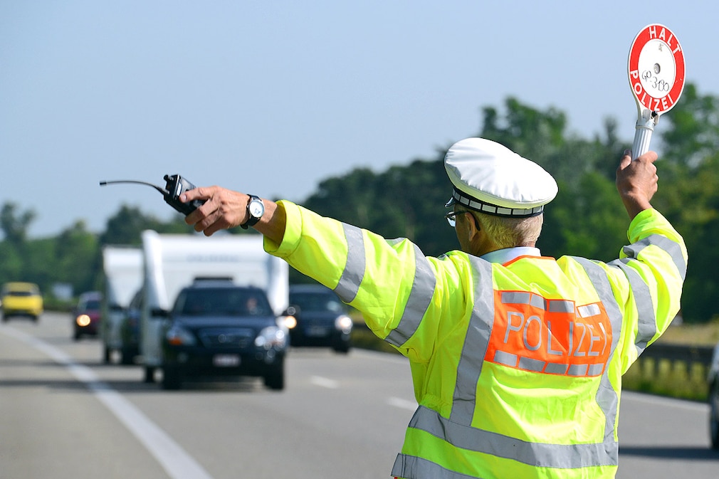 Ein Polizeibeamter winkt am 15.07.2013 an der A5 bei Neuenburg ein Fahrzeug mit einem Wohnanhänger zur Wiegekontrolle auf einen Parkplatz