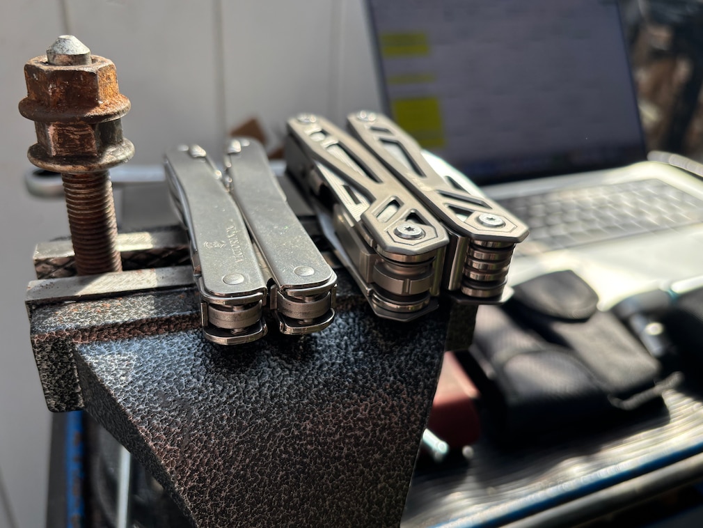 Perspektive: Größenvergleich eines schlanken und eines stärkeren Multitools, liegend auf einem Schraubstock.