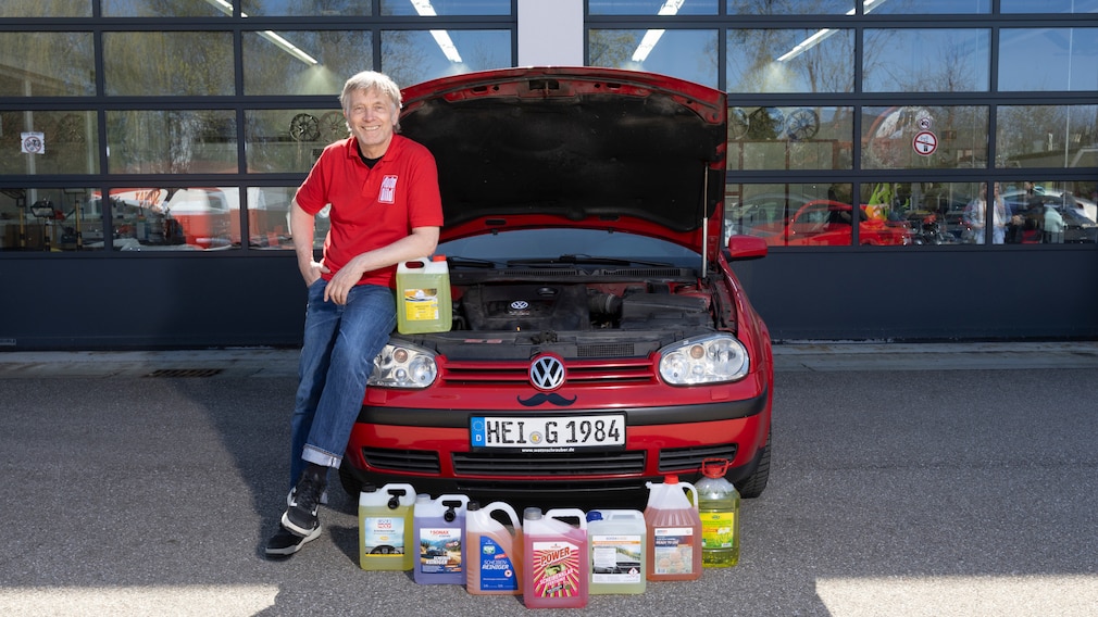 Person steht neben Auto mit offener Motorhaube, davor sind die Scheibenreiniger-Kanister aufgereiht.
