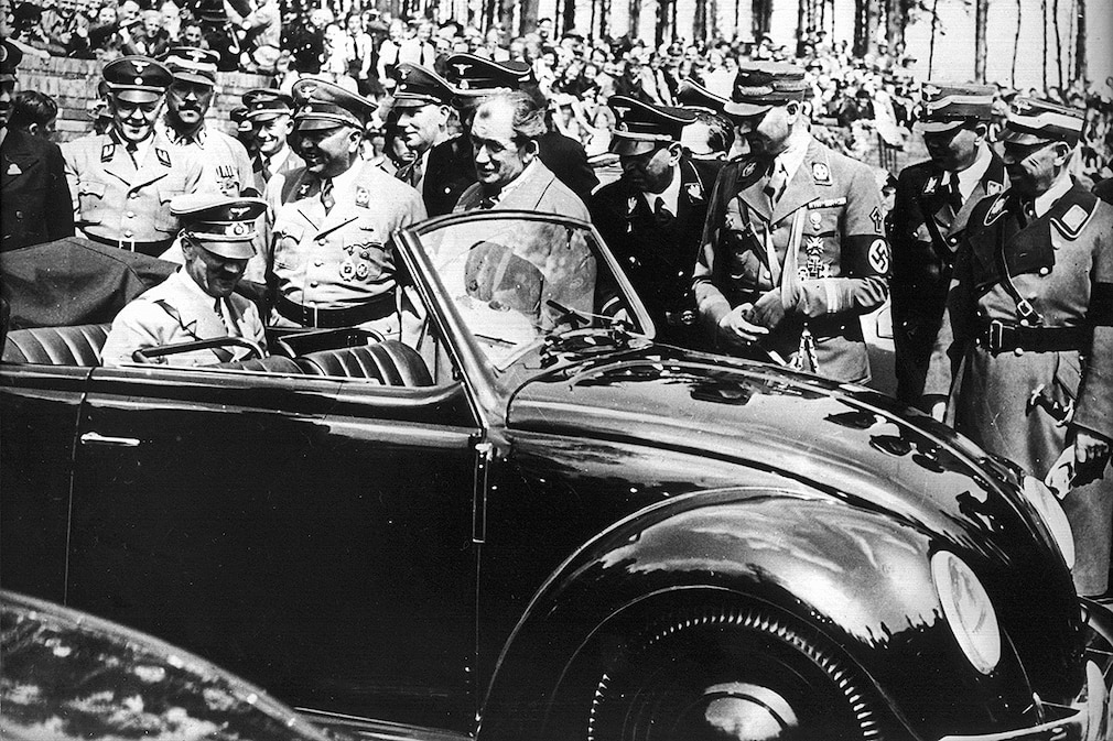 Adolf Hitler begutachtet auf der Rückbank sitzend den ersten Wagen vom Typ Käfer, der 1936 bei der "Gesellschaft zur Vorbereitung des deutschen Volkswagens" in Stuttgart nach den Entwürfen des Automobilkonstrukteurs Ferdinand Porsche (M, ohne Kopfbedeckung) gebaut wurde. Undatierte Aufnahme.