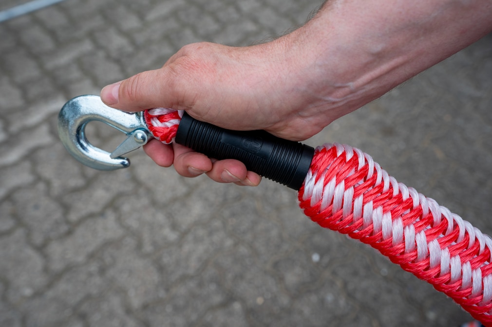 Hand zeigt Karabinerhaken an einem Abschleppseil.