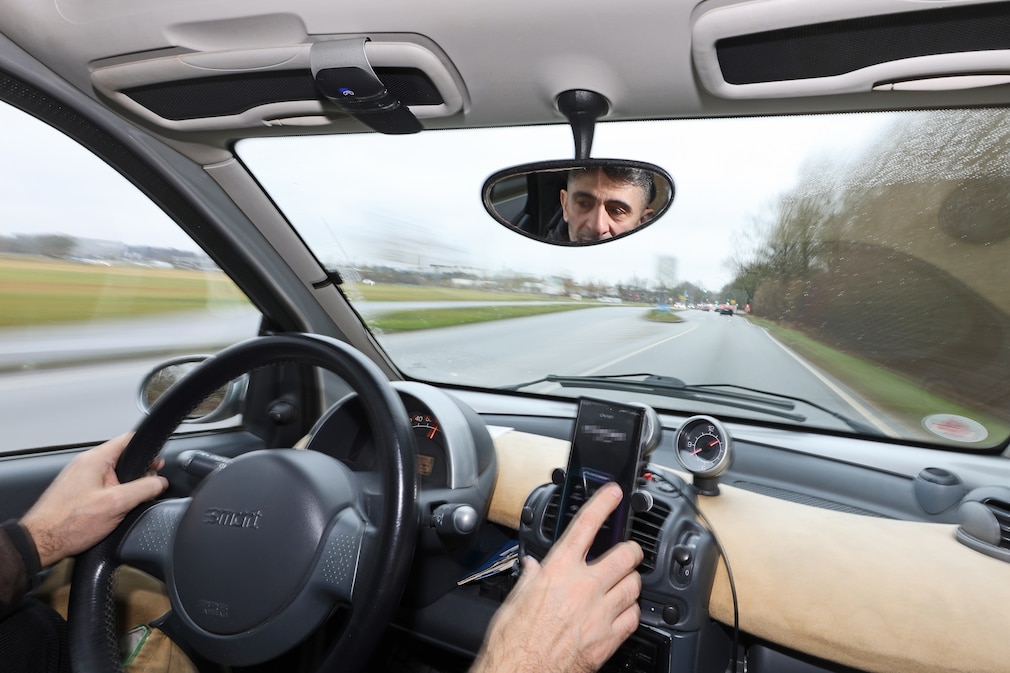 Eine Person sitzt im Auto und bedient das Smartphone, gehalten in einer Halterung, während der Fahrt.