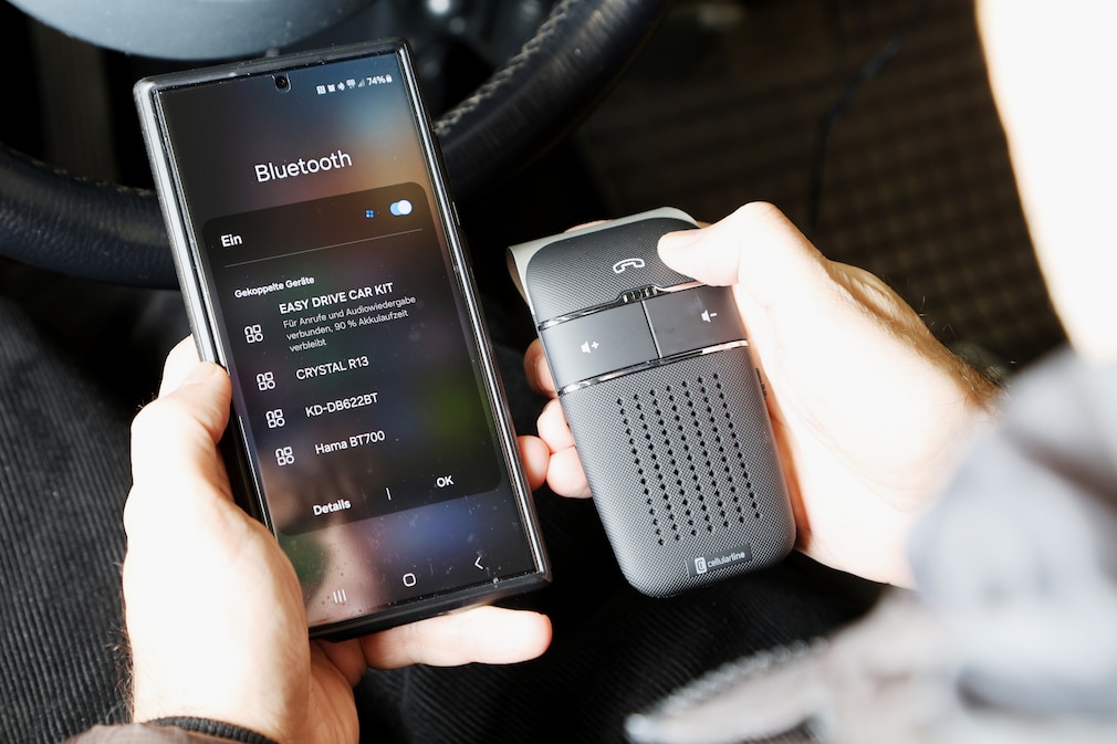 Testsituation: Eine Person hält Bluetooth-Freisprecheinrichtung und Smartphone zum Koppeln nebeneinander.