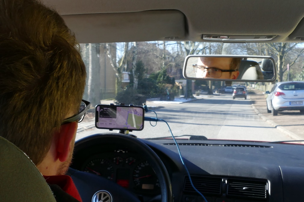 Blick von hinten auf Fahrer und Cockpit während der Fahrt. Handy und Halterung im direkten Sichtfeld an der Frontscheibe