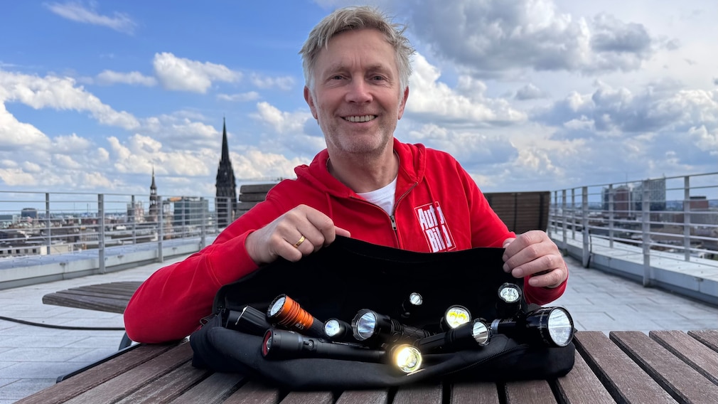 Eine Person hält bei Dunkelheit eine Klarsichtplatiktüte mit vielen leuchtenden Taschenlampen in die Höhe.
