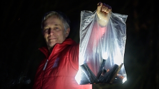 Eine Person hält bei Dunkelheit eine Klarsichtplatiktüte mit vielen leuchtenden Taschenlampen in die Höhe.