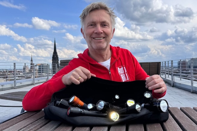 Eine Person hält bei Dunkelheit eine Klarsichtplatiktüte mit vielen leuchtenden Taschenlampen in die Höhe.