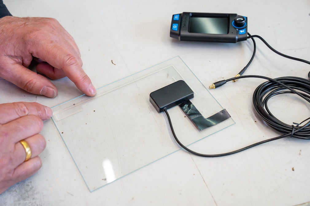 Montageszene: eine Person befestigt die Folienantenne eines DAB+-Adapters an einer kleinen, transportablen Glasscheibe.