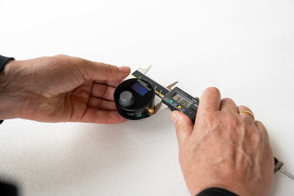 Nahaufnahme: Vermessungsszene eines DAB+-Adapters mit Messschieber vor neutralem Hintergrund