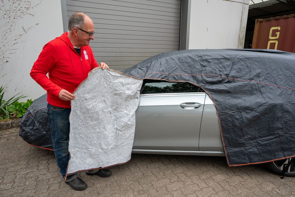 Eine Person hält am Fahrzeug den geöffneten Zugang durch die Plane zur Fahrertür auf.