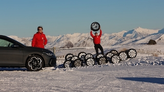 Redakteure stehen vor einer Reihe Reifen, ein Redakteur hebt einen Reifen an. An der Seite steht ein grauer VW Golf