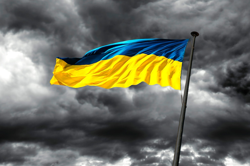 Eine ukrainische Flagge flattert vor dunklem Wolkenhimmel im Wind.