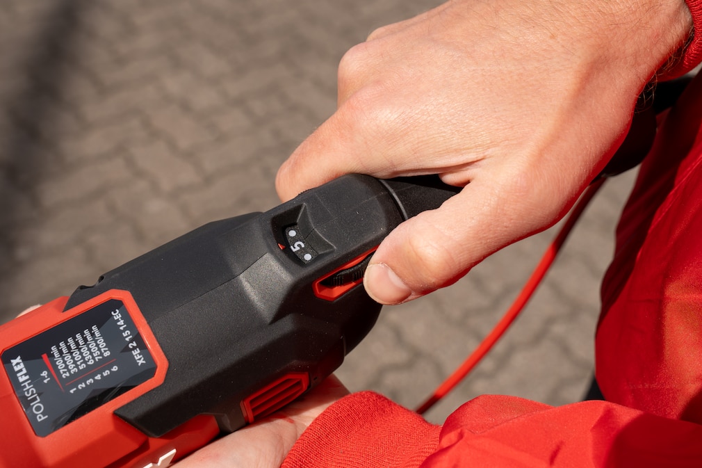 Poliermaschine wird am Griff in der Hand gehalten, Fokus liegt auf dem Drehzahleinstellrädchen.
