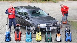 2 Personen stehen an einem Fahrzeug, vor dem einige Hochdruckreiniger aufgereiht sind. Die eine Person betätigt die Pistole eines Hochdruckreinigers, die andere hantiert an dem dazu zugehörigen Gerät