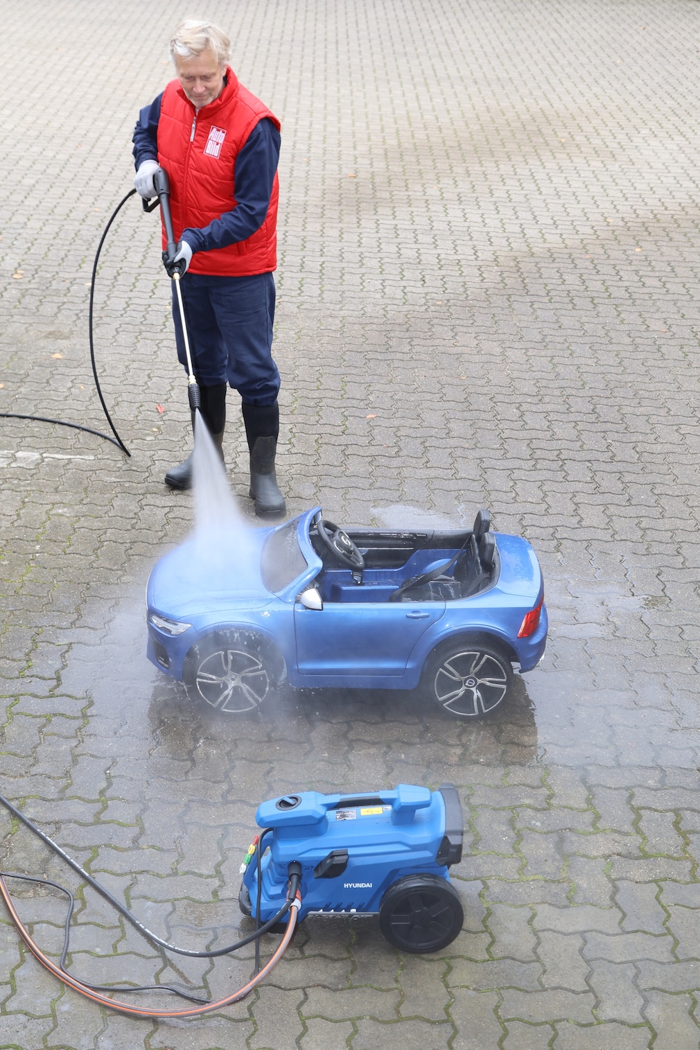 Eine Person reinigt mit dem einzigen, im Liegen benutzbaren, Hochdruckreiniger von Hyundai ein ähnlich großes Spielzeugauto.