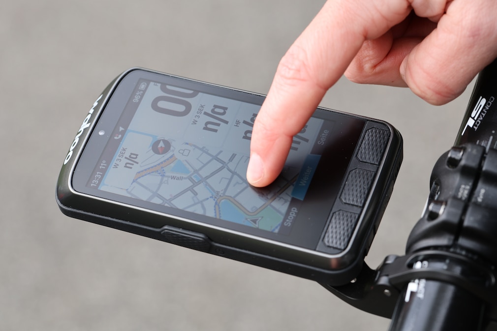 Nahaufnahme: Eine Hand bedient einen montierten Fahrradcomputer.