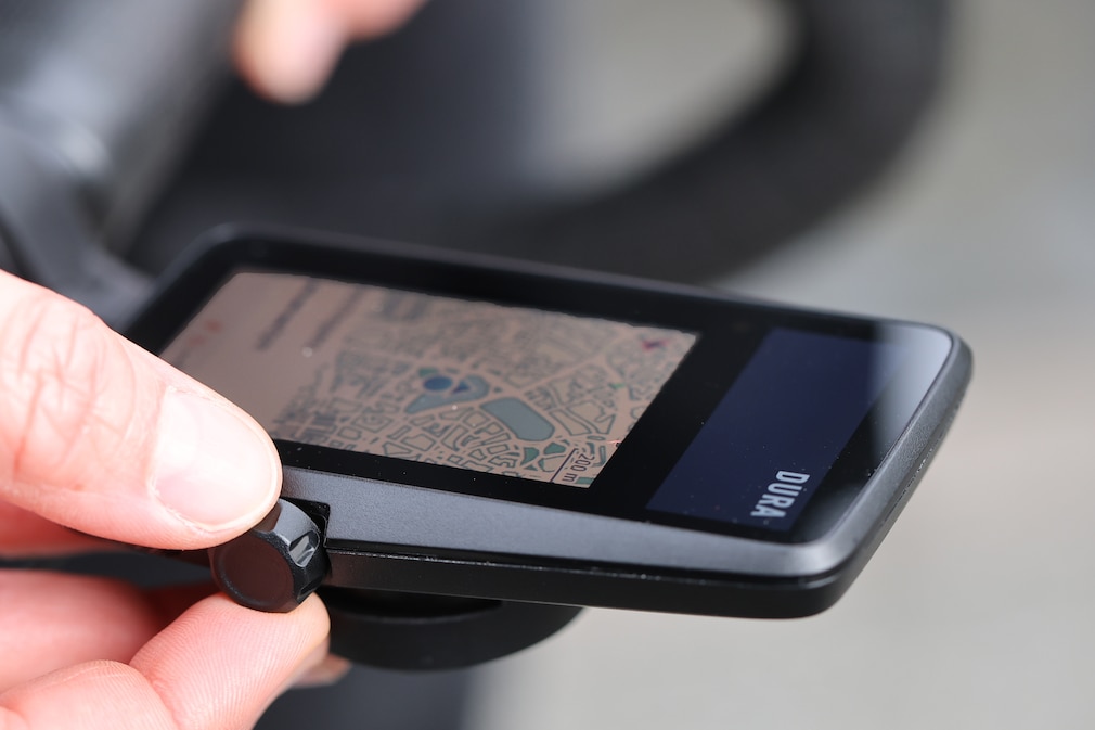 Nahaufnahme mit Sicht auf die Kartendarstellung: Eine Hand bedient einen montierten Fahrradcomputer.