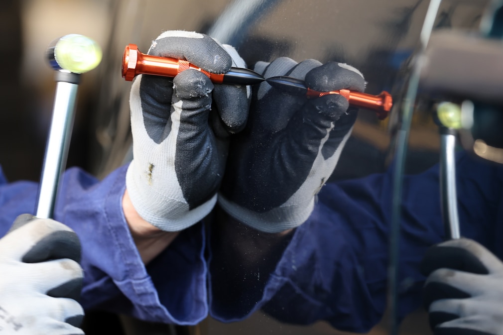 Nahaufnahme: Arbeit mit Hammer und Beulenstift an einem Karosserieteil.