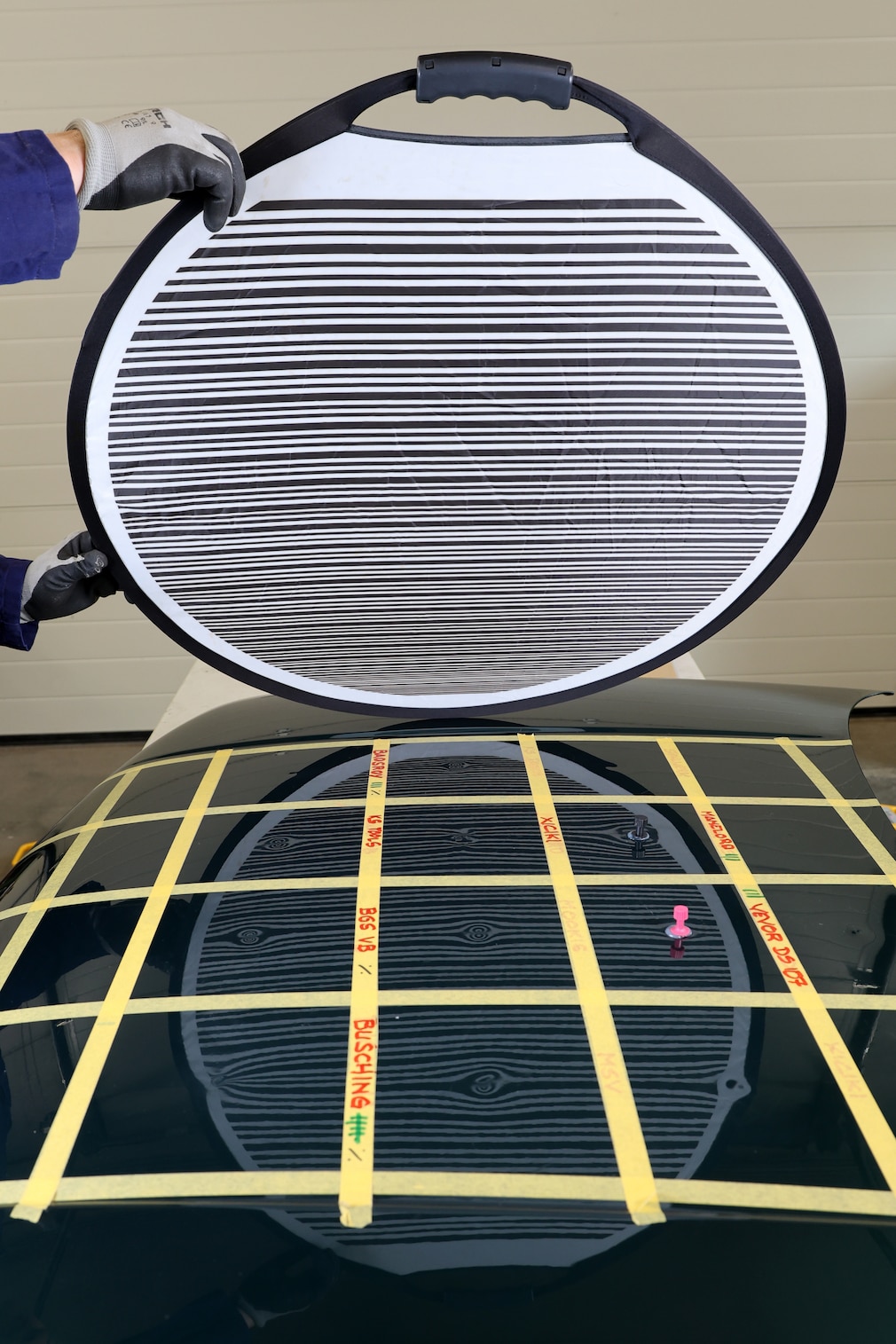 Reflektor-Board, gehalten über einer in Felder eingeteilten Motorhaube, um die Verformungen im Blech sichtbar zu machen.