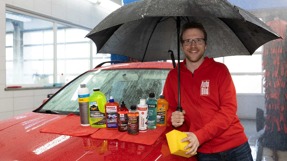 Redakteur in AUTO BILD-Jacke steht unterm Regenschirm neben einem Auto in einer laufenden Waschanlage