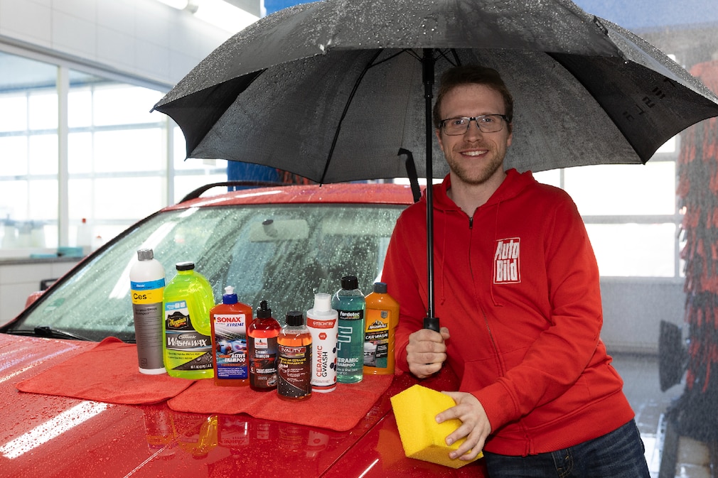 Redakteur in AUTO BILD-Jacke steht unterm Regenschirm neben einem Auto in einer laufenden Waschanlage