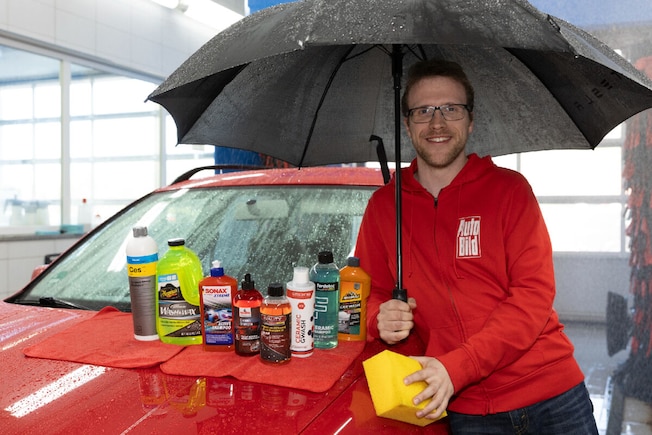 Redakteur in AUTO BILD-Jacke steht unterm Regenschirm neben einem Auto in einer laufenden Waschanlage