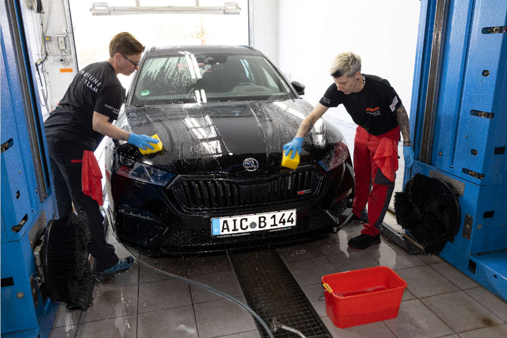Zwei Menschen waschen die Motorhaube eines schwarzen Skoda Octavia.