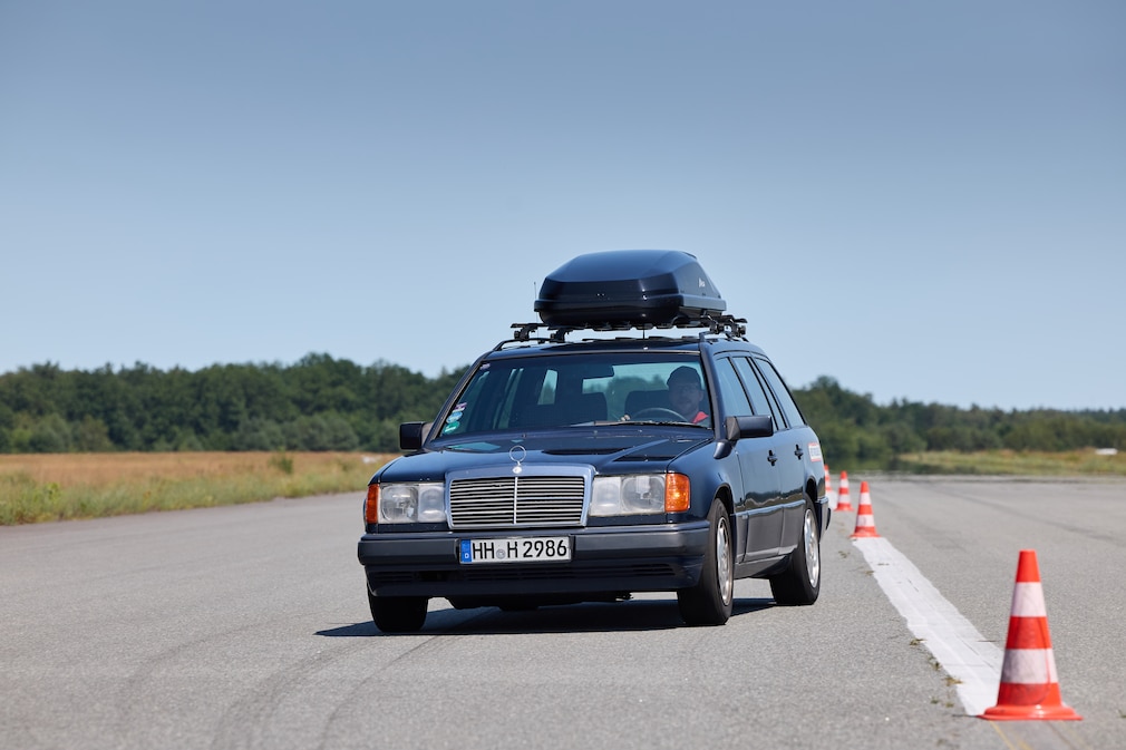 Blauer Mercedes 300 TE der Baureihe W124 mit Dachbox fährt einen Slalom.