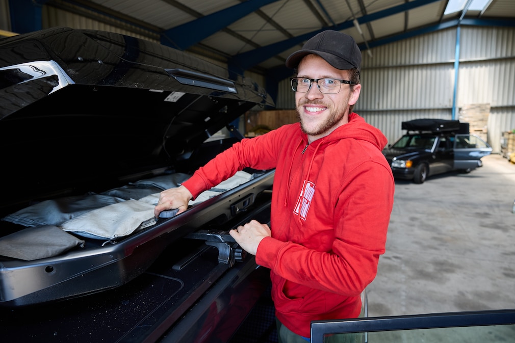 Eine Person bei der Montage an geöffneter Dachbox auf Fahrzeugdach