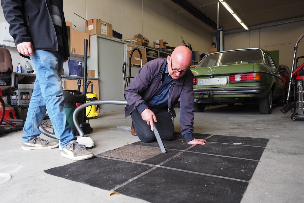 Werkstattsituation: eine Person arbeitet mit einem Sauger, kniend auf einer in mehrere Flächen unterteilten Versuchsfläche.
