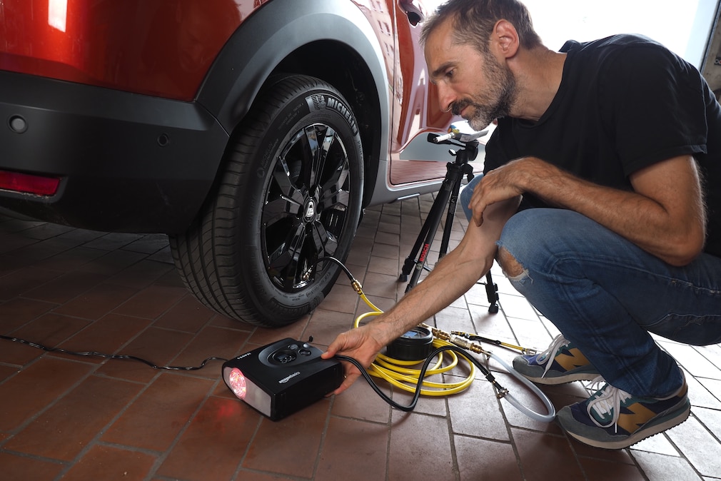 Eine Person kniet am Vorderrad neben einem Fahrzeug mit einem angeschlossenen 12V-Kompressor.