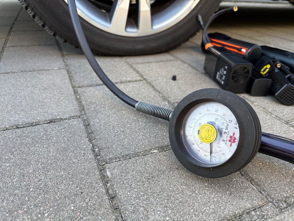 Nahaufnahme von angeschlossenenem Reifendruckprüfer an Fahrzeugvorderrad.