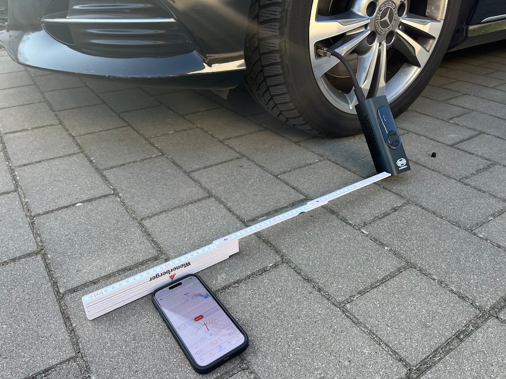 Testsituation: Phonmessung der Akku-Luftpumpen-Lautstärke in definiertem Abstand mit Messgerät und Akku-Pumpe vor Fahrzeugvorderrad.