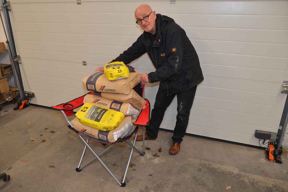 Testsituation: eine Person bepackt einen Campingstuhl mit Gewichten (Zementsäcken) in einer Garage, um die Maximallast zu prüfen.