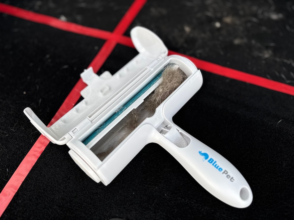 Produktfoto: ein Tierhaarentferner liegt mit aufgeklapptem und mit Tierhaaren gefülltem Auffangbehälter auf der damit gereinigten Testfläche.