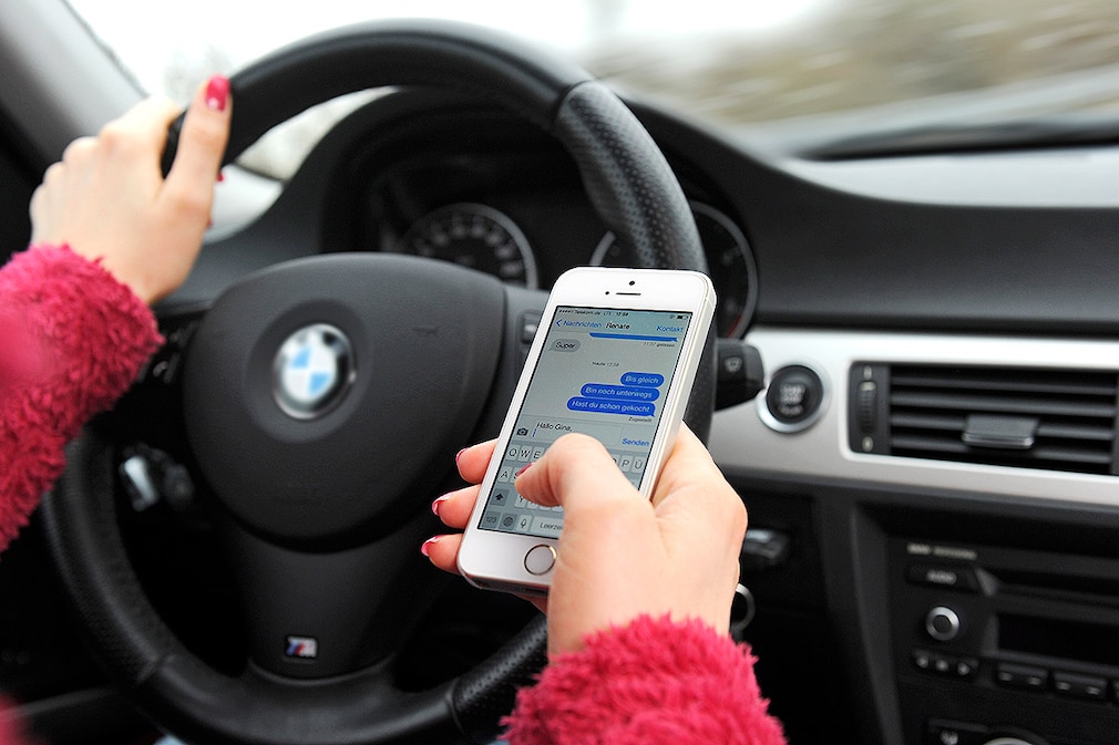 Handy am Steuer - Frau schreibt während der Autofahrt eine SMS.