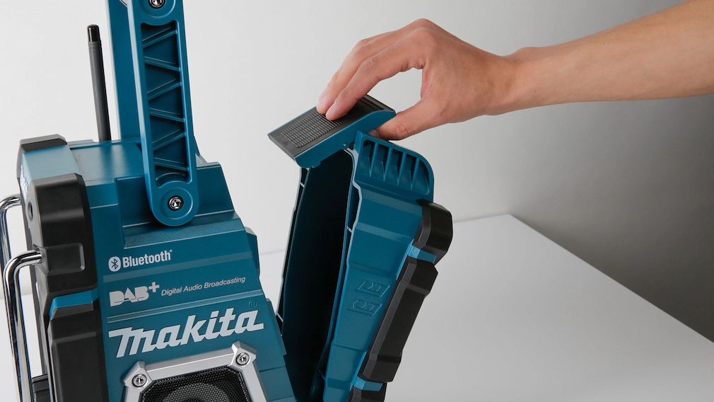 Detailaufnahme des Makita-Baustellenradios. Eine Hand öffnet eine Klappe am Gerät