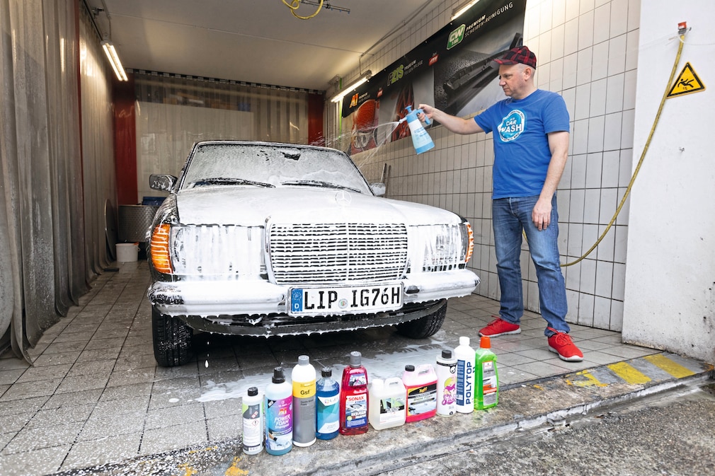 Person beim Einsprühen eines Fahrzeugs mit Snow Foam Shampoo in Waschbox.