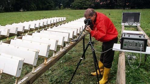 Eine Person schaut mithilfe eines Endoskops in die Testbehälter, aufgereiht auf einer Wiese.
