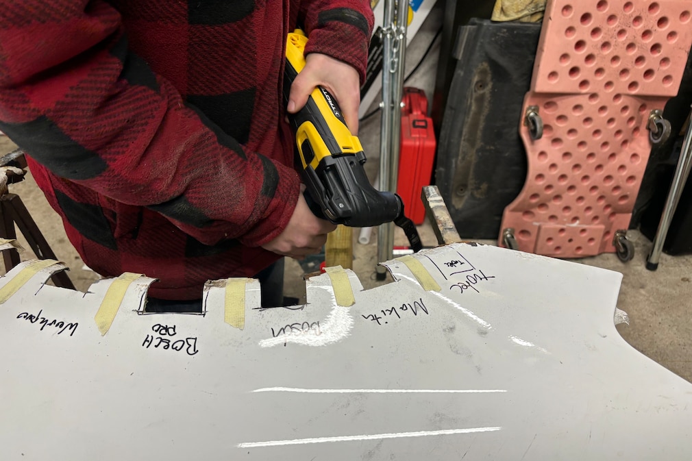 Testsituation: Perspektive auf den Versuchsaufbau. Eine Person sägt mit einem Multitool ein Blechstück aus dem dafür markierten Autoblech.