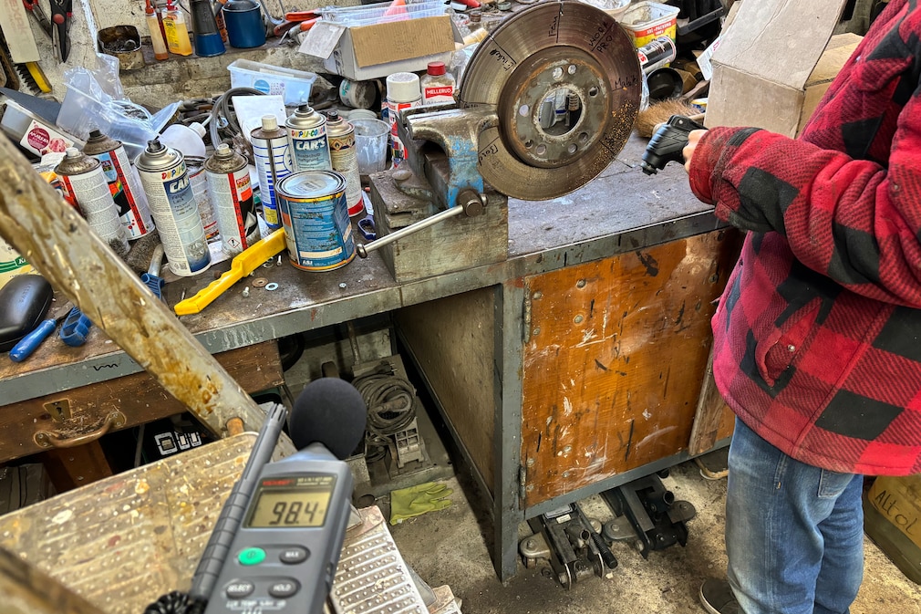 Werkstattsituation: Lautstärkemessung mit Phonmessgerät, während eine Person mit einem Multitool Schnittversuche an einer Bremsscheibe macht.