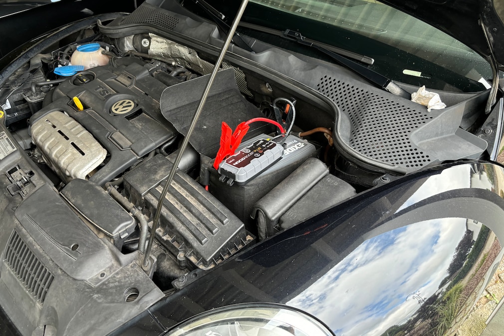 Geöffnete Motorhaube: Starthilfegerät angeschlossen an Autobatterie.
