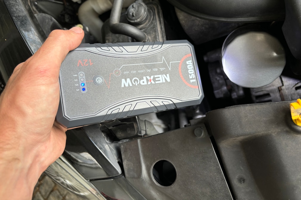 Hand hält Starthilfegerät in einen Motorraum und demonstriert die integrierte Taschenlampenfunktion.