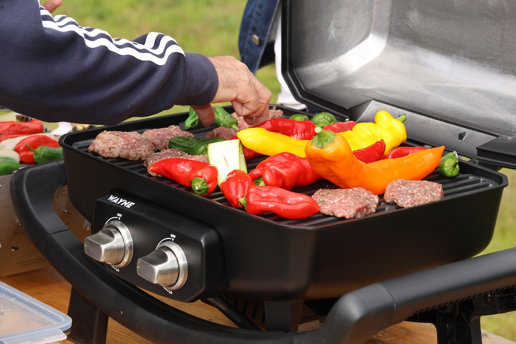 Perspektive auf den mit Fleisch und buntem Gemüse belegten Camping-Gasgrill von Burnhard Wayne.
