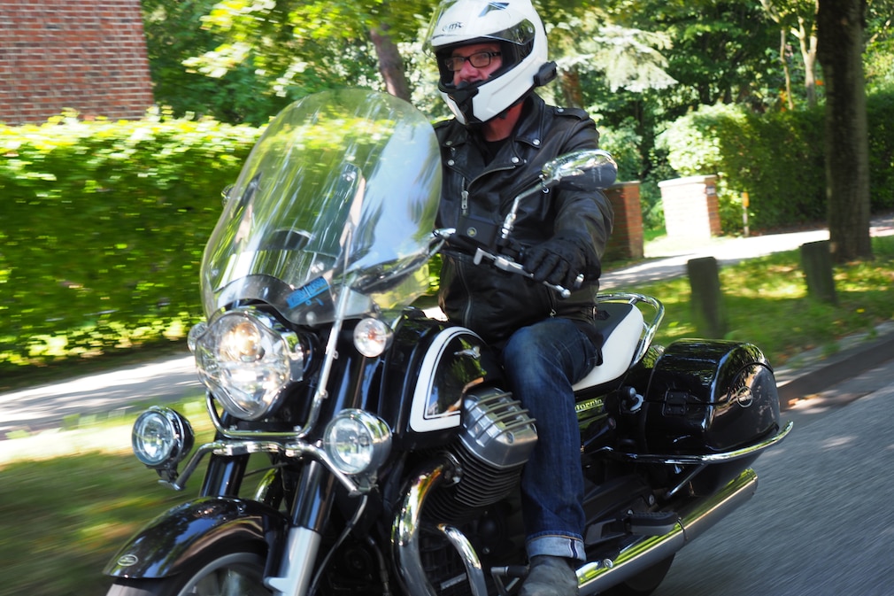 Ein Motorrad schräg von vorn im Strassenverkehr. Am Helm des Fahrers ist deutlich sichtbar ein Headset angebracht.