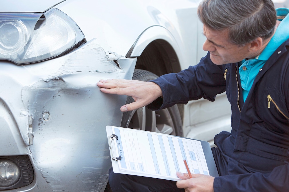 Auto Workshop Mechanic Inspecting Damage To Car