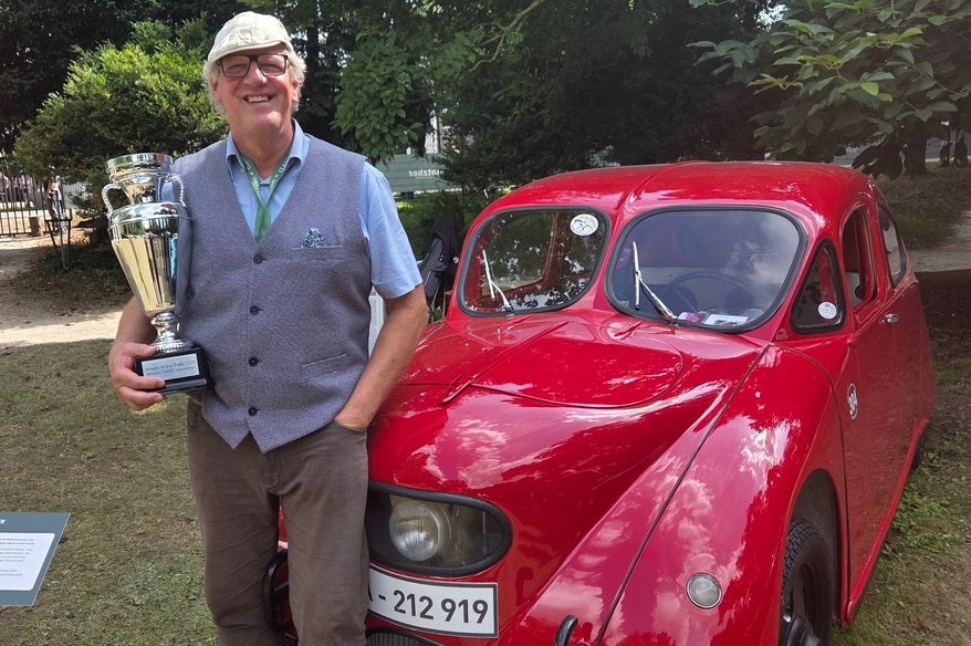 Jörg Jansen, ein Mann um die 60, am Auto, mit großem Pokal auf dem Arm