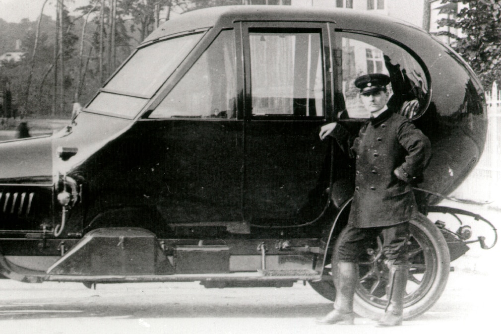 Detail aus dem Foto oben: Mann steht am eiförmigen Heck des Automobils von 1912.